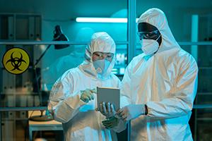 两个穿着防护服的人在实验室里，身后挂着生物安全标志.
